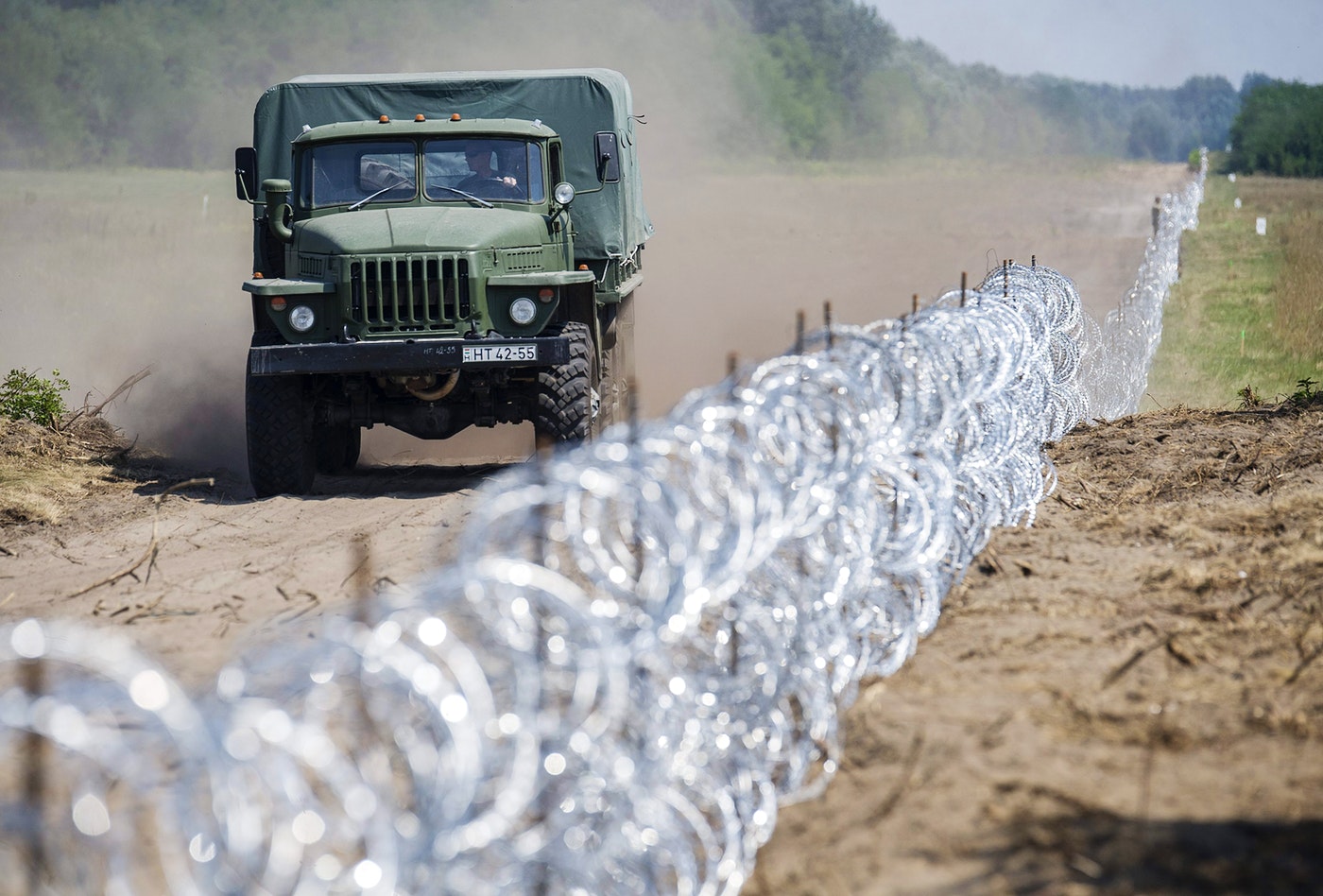 A Hungarian military truck passes a barbed-wire section of a 108-mile (175km) fence on Hungary’s southern border with Serbia near Kelebia, 110 miles (178 km) southeast of Budapest, Hungary, on Friday, Aug. 7, 2015. (Sandor Ujvari/MTI via AP)
