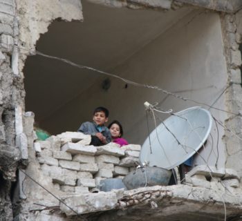 In this Thursday, Feb. 11, 2016 photo, children peer from a partially destroyed home in Aleppo, Syria. The fighting around Syria's largest city of Aleppo has brought government forces closer to the Turkish border than at any point in recent years, routing rebels from key areas and creating a humanitarian disaster as tens of thousands of people flee. (Alexander Kots/Komsomolskaya Pravda via AP)