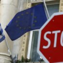The Greek (L) and European Union flags are seen behind a stop sign in front of the Greek embassy in Vienna, Austria, February 25, 2016.   REUTERS/Leonhard Foeger