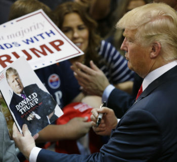 FILE - In this May 6, 2016 file photo, Republican presidential candidate Donald Trump looks at his photo on a magazine cover as he signs autographs during a rally in Eugene, Ore. The city of Eugene plans to bill the Donald Trump campaign nearly $100,000 to pay for costs associated with last month's visit. Police Chief Pete Kerns said in an email Wednesday, June 22, 2016, that overtime compensation for police officers totaled $78,000 while firefighters and other city employees racked up another $10,000 in OT. (AP Photo/Ted S. Warren, file)