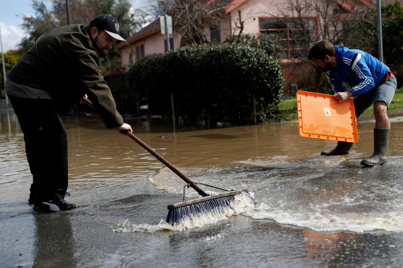 (L-R) Neighbors Alfredo Azevedo and Gordon Smith push flood water to a storm drain after Coyote Creek burst its banks and flooded nearby neighborhoods and prompted evacuation of more than 14,000 residents in San Jose, California. REUTERS/Stephen Lam